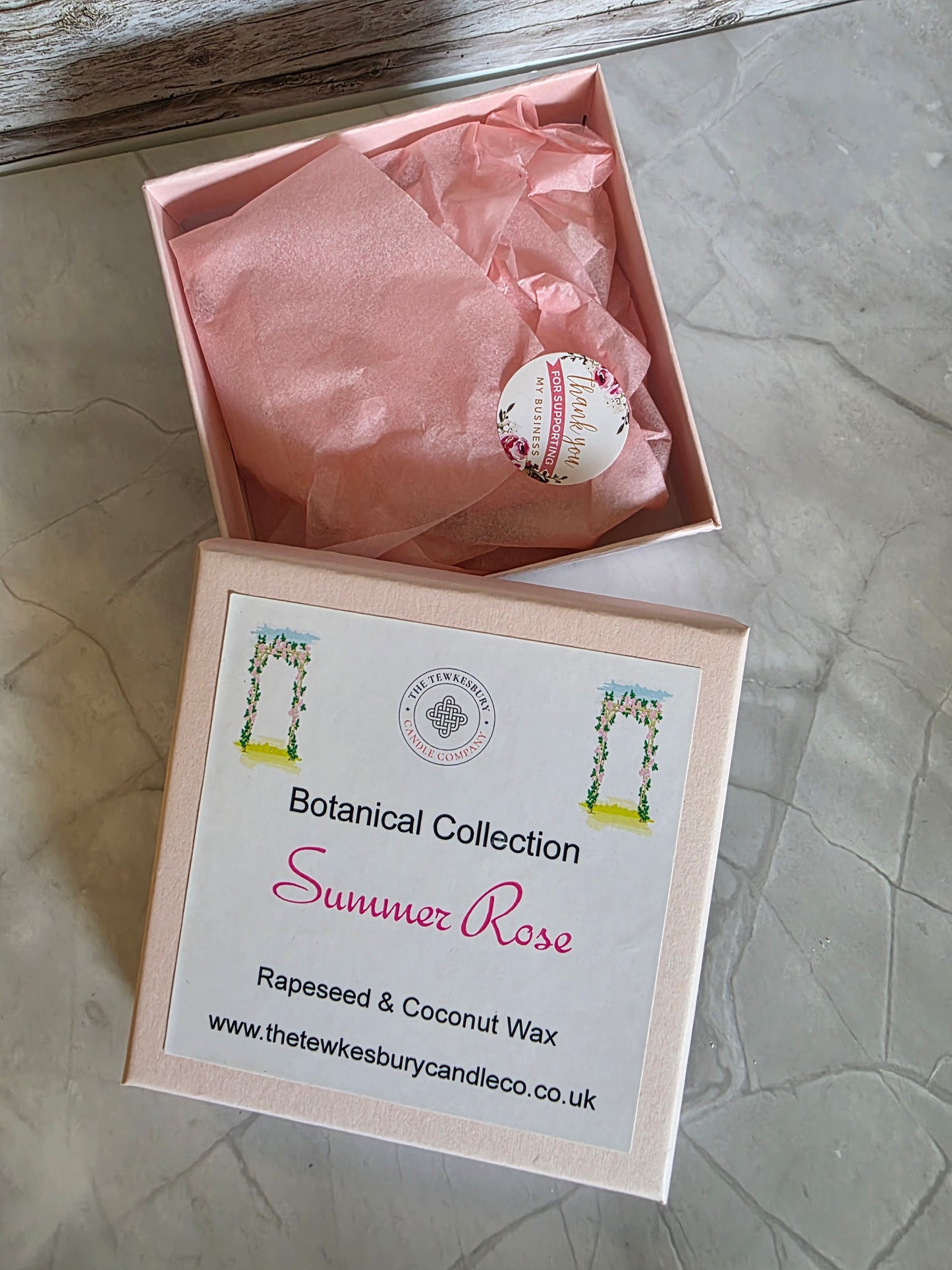 Box with pink tissue paper and a product labeled 'Summer Rose' on a textured surface.