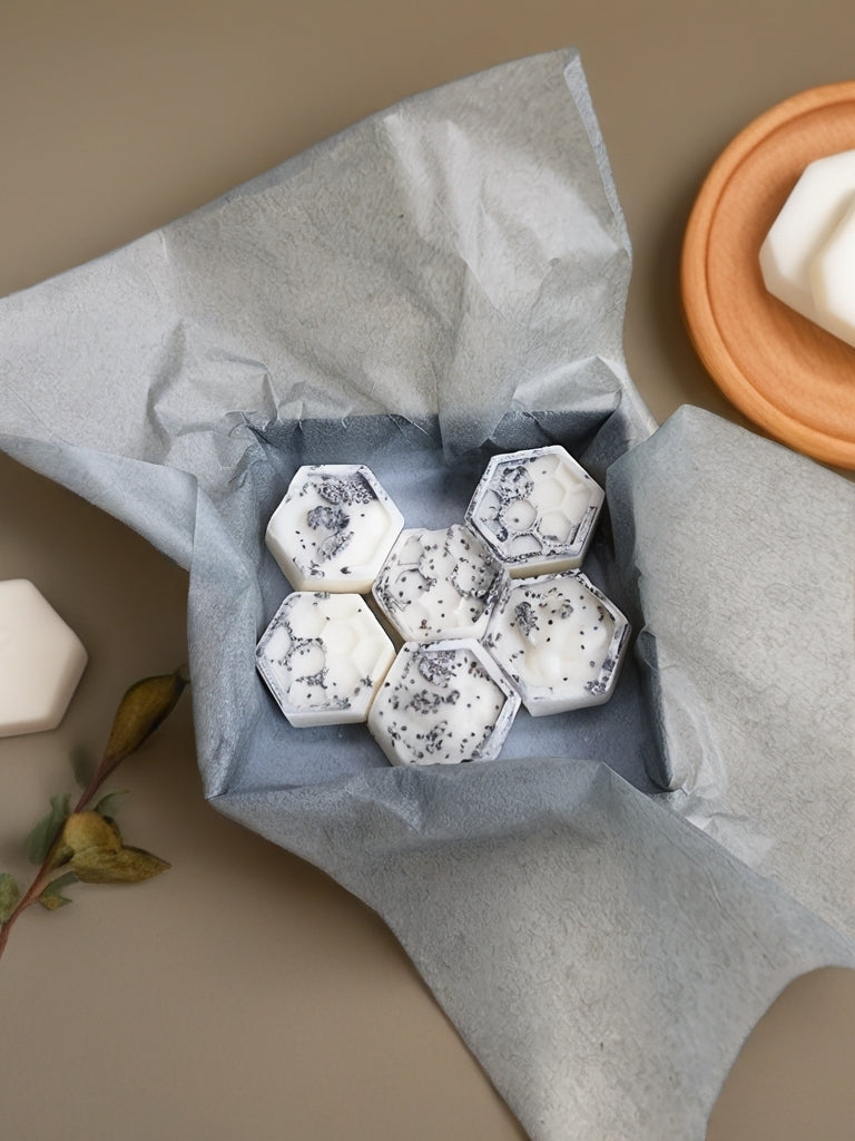 Hexagonal wax melts with a speckled pattern in a gray box on a beige surface.
