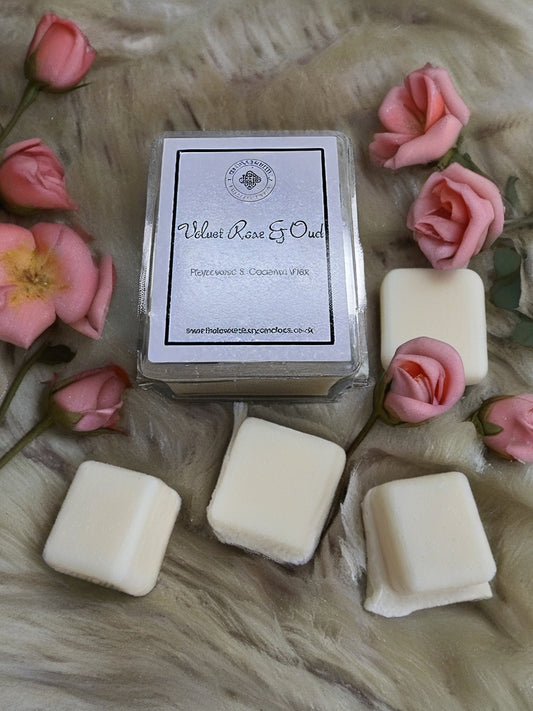A clamshell wax melt with a label surrounded by pink flowers on a textured surface